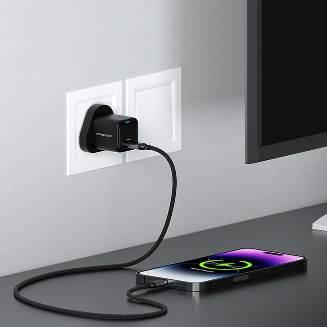 alt="A UK 3Pin Ultra-Compact Gan Charger plugged in the socket with charging cable, charging the smartphone"